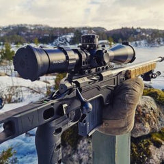 Close-up of a precision rifle with optical scope mounted, featuring the Deadline 2.0 Action in an outdoor snowy mountainous setting.