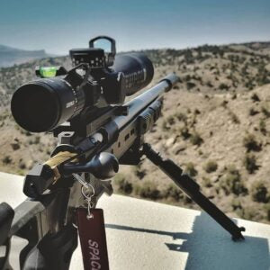 Close-up of a Deadline 2.0 Action rifle mounted on a bipod with scope, set against a desert landscape background during daylight.